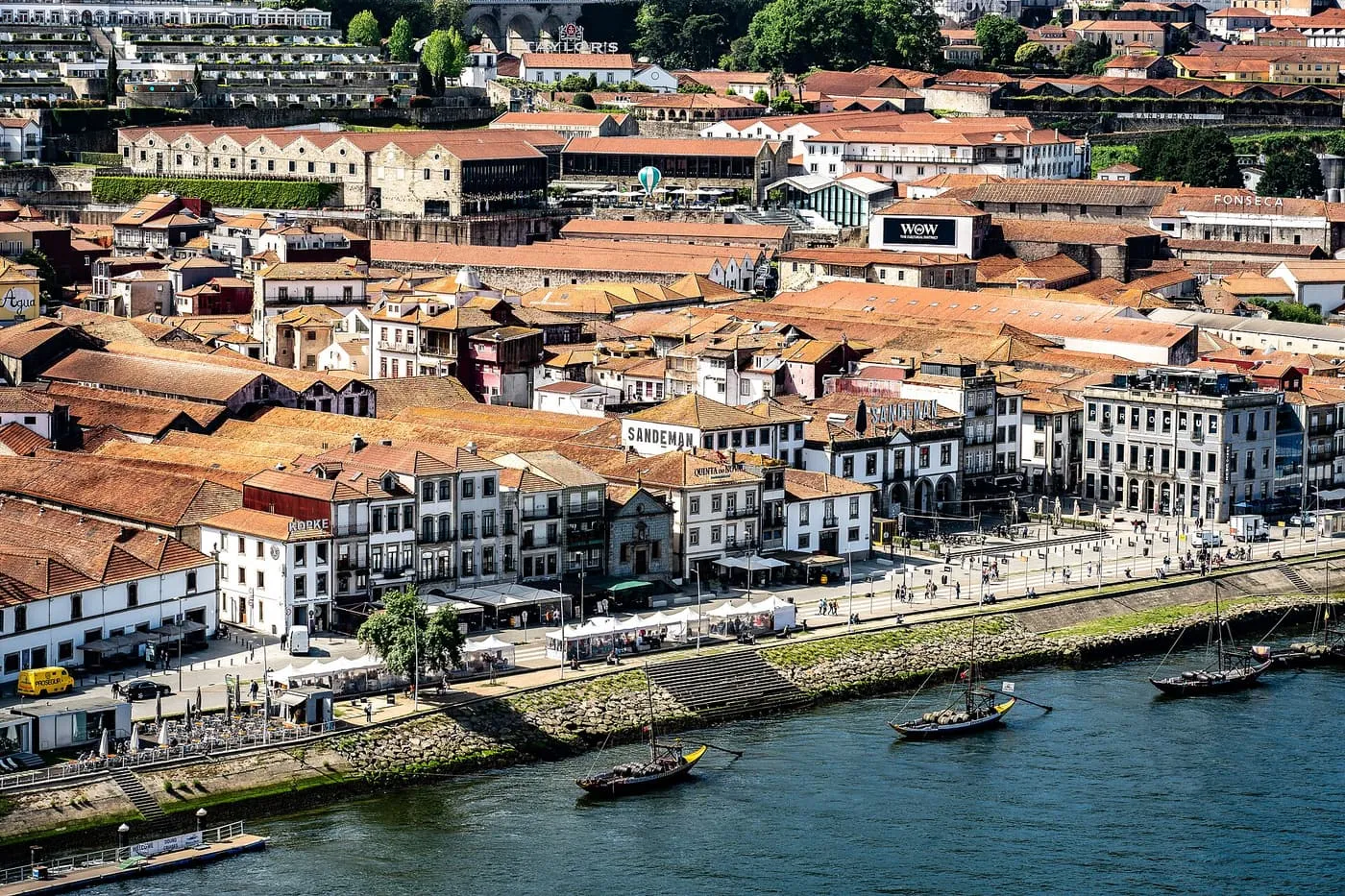 The Gaia waterfront seen from above, with terracotta-roofed port lodges carrying the Sandeman, Kopke and Fonseca signs and rabelo boats moored on the Douro