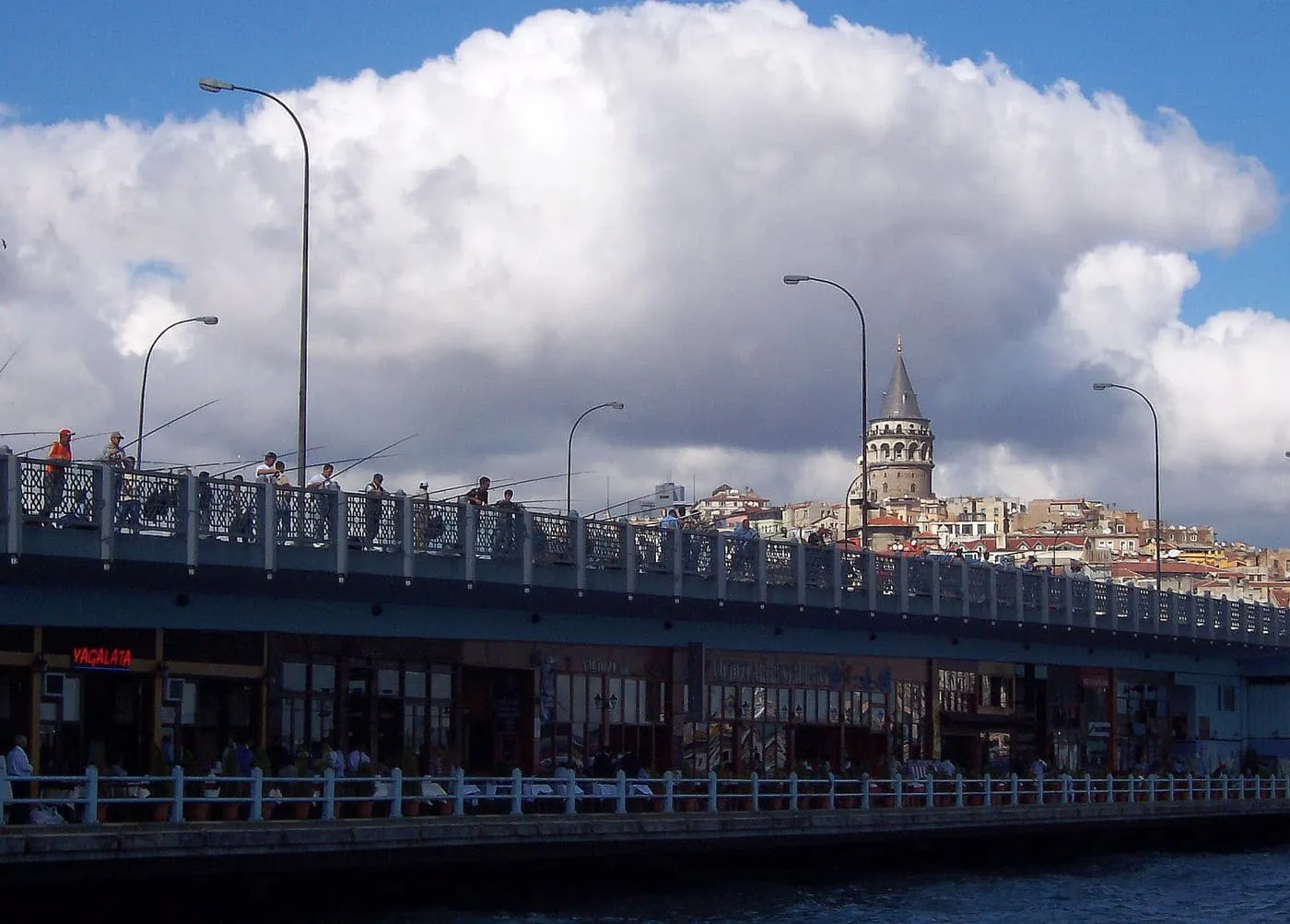 The Galata Bridge with fishermen along its upper rail and restaurants below, and the Galata Tower on the hill beyond