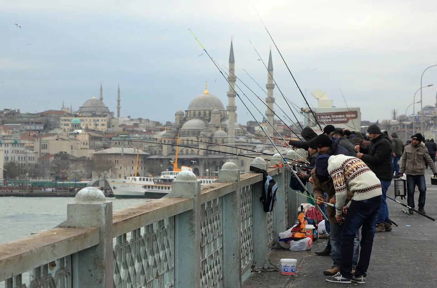 Fishermen lining the railing of the Galata Bridge with rods out over the Golden Horn and the Yeni Cami behind