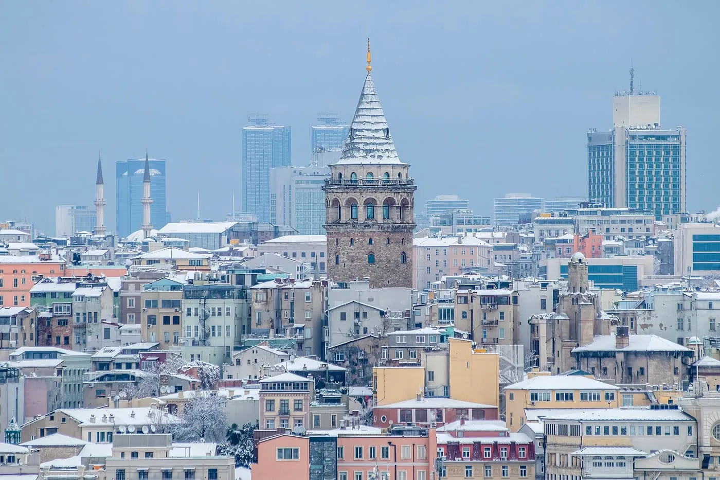 The Galata Tower and the roofs of Beyoğlu dusted with snow under a pale blue sky