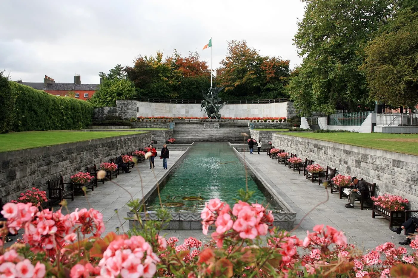 The long rectangular pool of the Garden of Remembrance with benches along both sides, a sculpture at the far end and an Irish flag