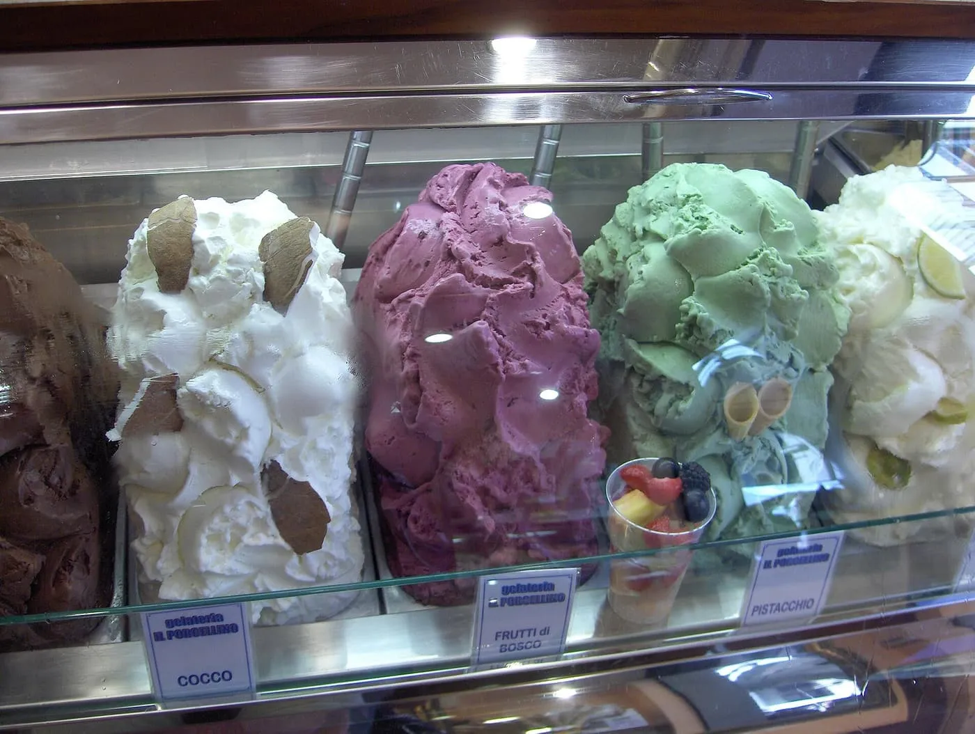 Tubs of gelato heaped behind glass, among them coconut, wild berry and pistachio, with a cup of fruit beside them