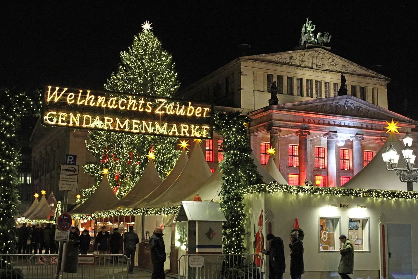 White market tents and a lit Christmas tree at night in front of the Konzerthaus on Gendarmenmarkt