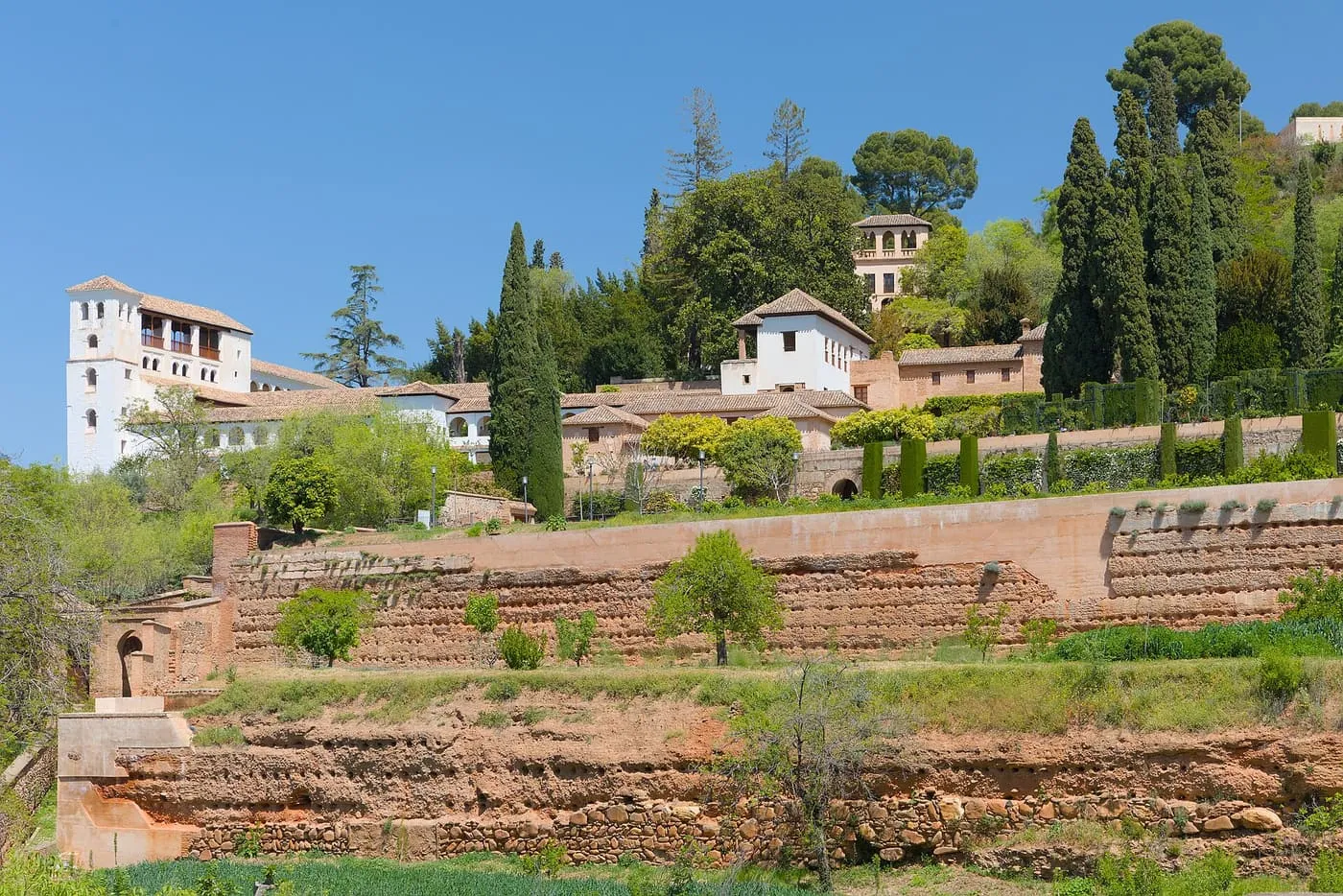 The white buildings of the Generalife on a wooded hillside above terraced garden walls and cypresses