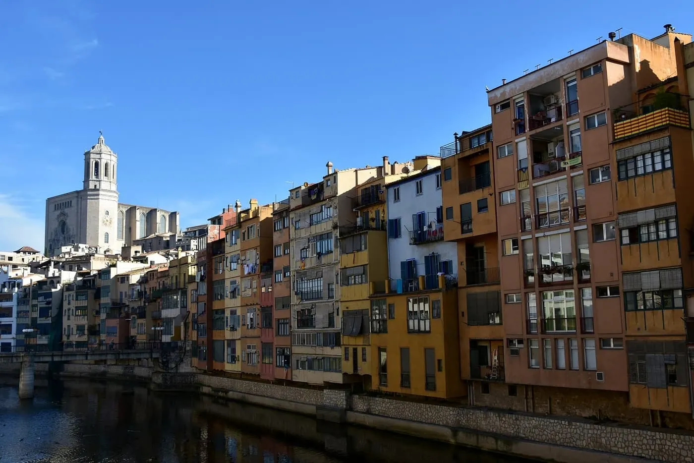 Tall ochre, orange and white houses lining the River Onyar in Girona, with the cathedral's bell tower rising behind