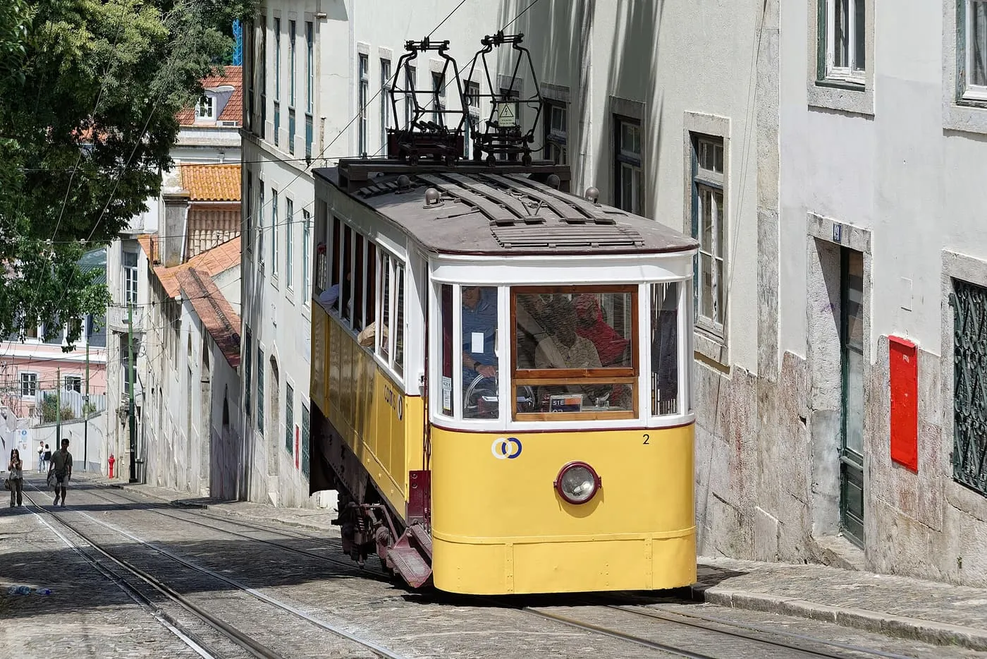A yellow Glória funicular car climbing a steep cobbled street between white buildings