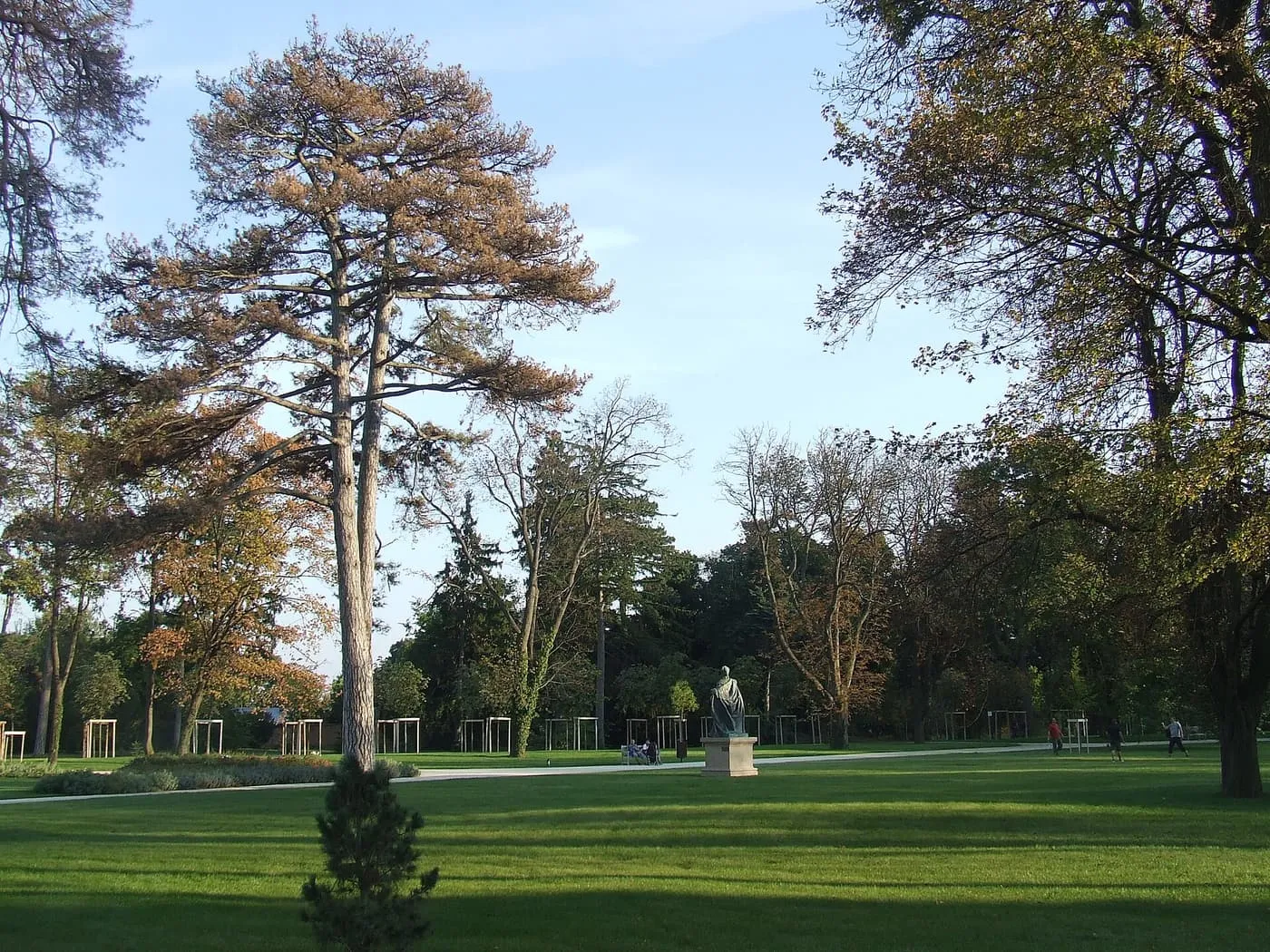Lawns and tall trees in the park of the Royal Palace at Gödöllő, with a statue beside a path