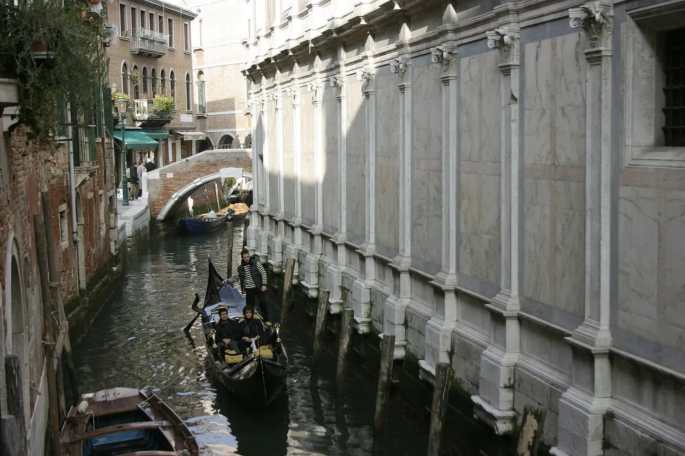 A gondola on a narrow canal beside the marble wall of Santa Maria dei Miracoli
