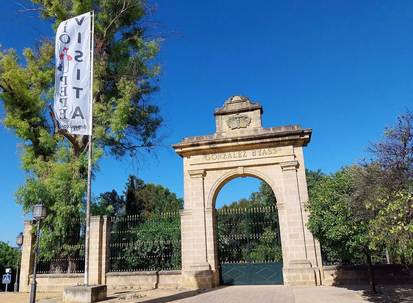 The stone entrance arch of the González Byass bodega in Jerez, with the family name over the archway and a Tío Pepe visitor flag beside it