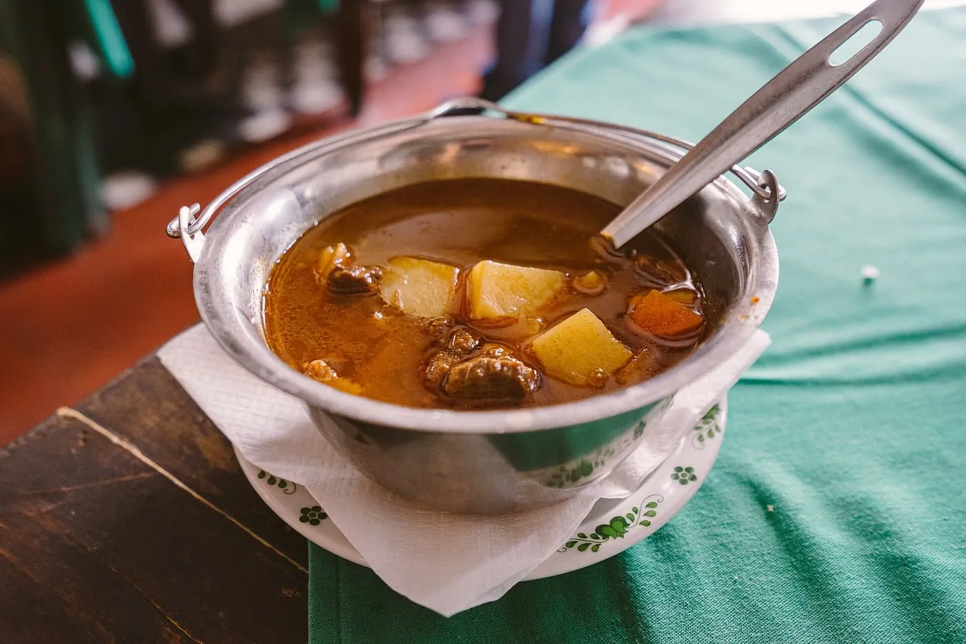 Goulash with beef and potato in a small metal kettle-shaped bowl on a green tablecloth