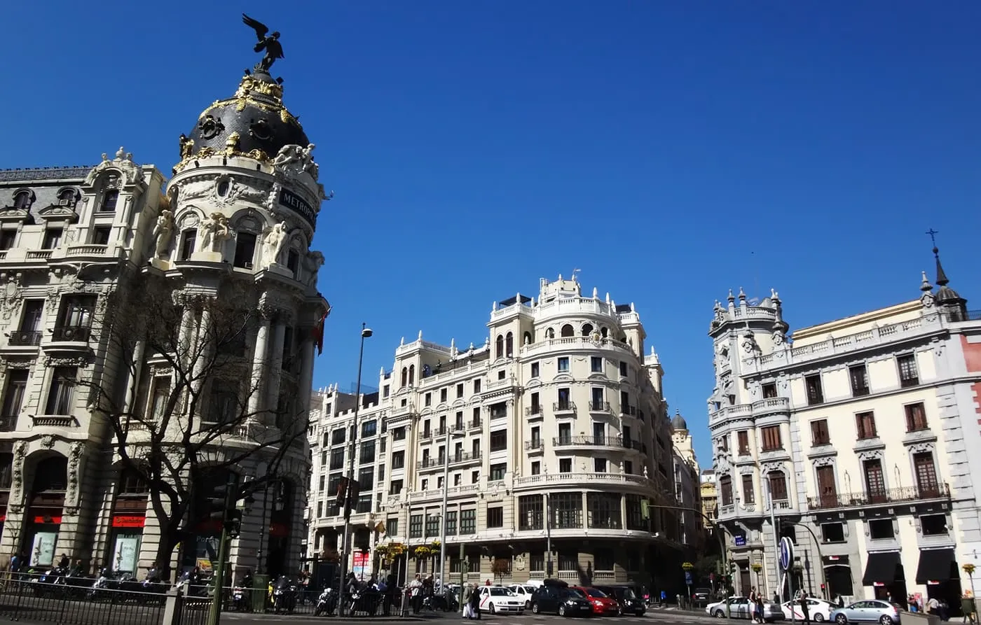 The domed corner tower of the Metrópolis building at the start of the Gran Vía, with other white stone buildings beside it under a blue sky