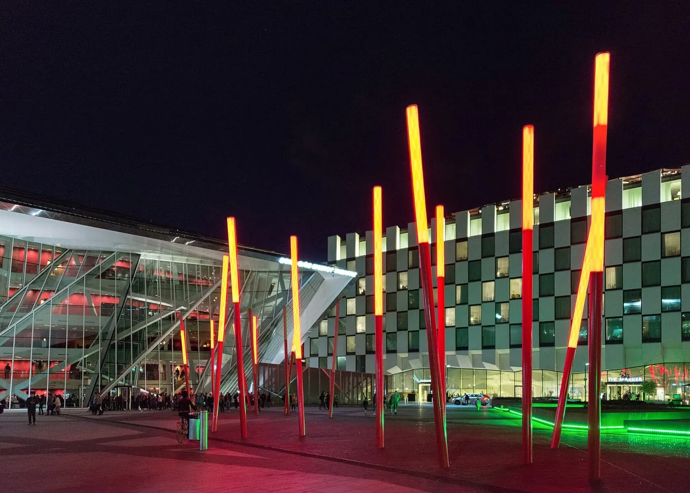 Red light columns on Grand Canal Square at night, with the glass-fronted theatre on the left and a chequerboard-fronted hotel on the right