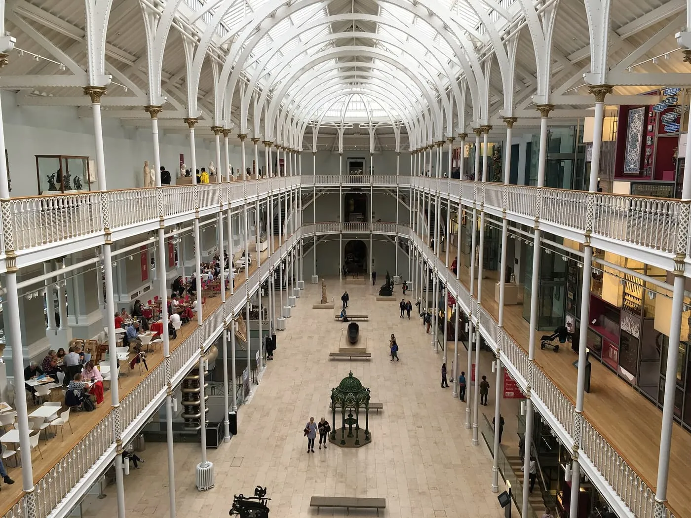 The Grand Gallery of the National Museum of Scotland seen from a balcony, with white iron columns, galleries on three levels and a glass roof
