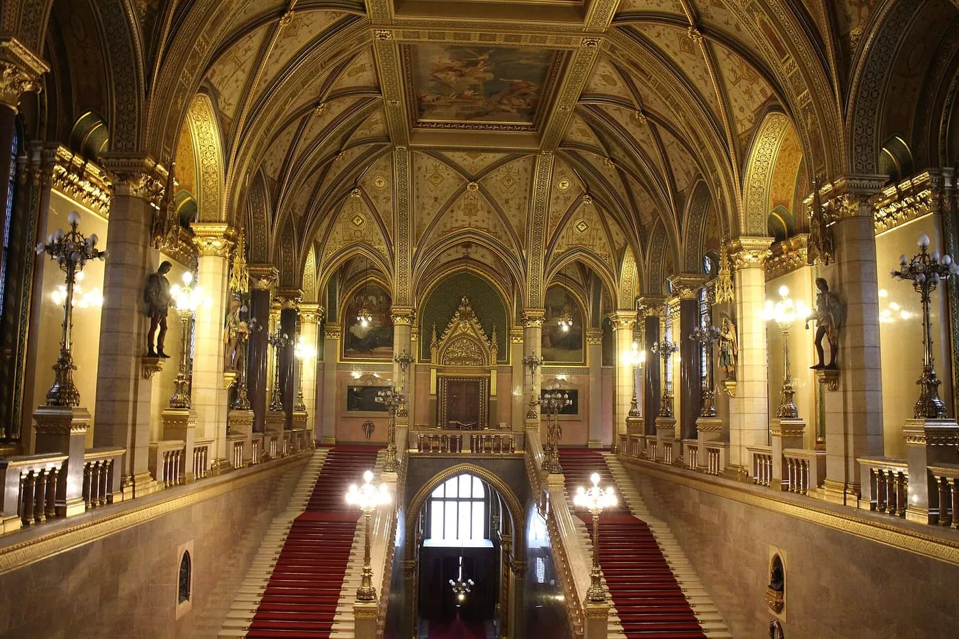 The Grand Stairway of the Hungarian Parliament, with red carpet on both flights and a gilded vaulted ceiling above