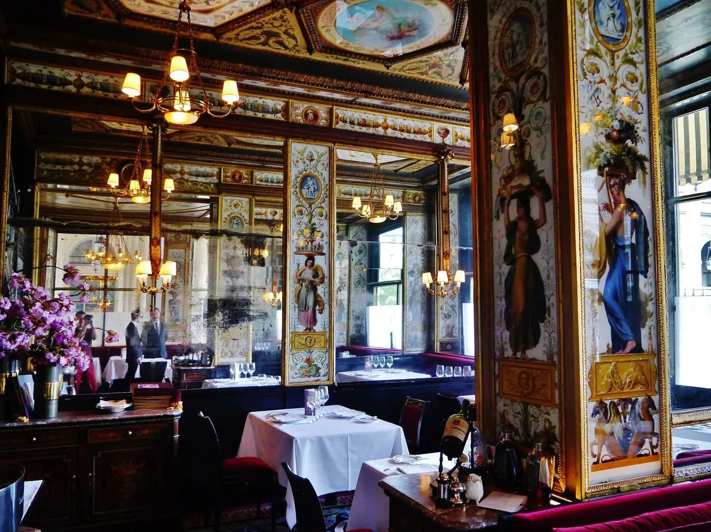 The painted and gilded panels, mirrors and chandeliers of the Grand Véfour dining room, with white-clothed tables and red velvet seats