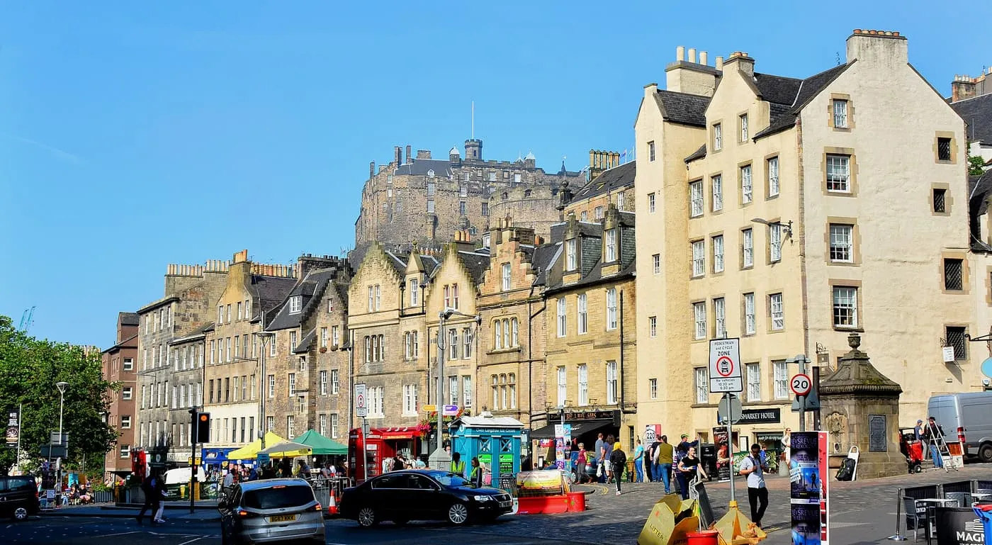 Cream and stone buildings around the Grassmarket under a blue sky, with Edinburgh Castle rising behind the rooftops