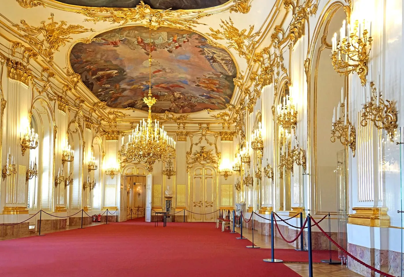 The Great Gallery at Schönbrunn, a long white and gold hall with a painted ceiling, chandeliers and a red carpet