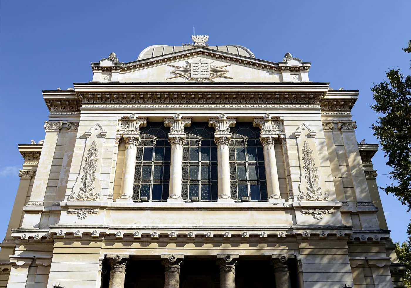 The front of the Great Synagogue of Rome, a pale stone building with a pediment, a tall arched window and a low dome behind