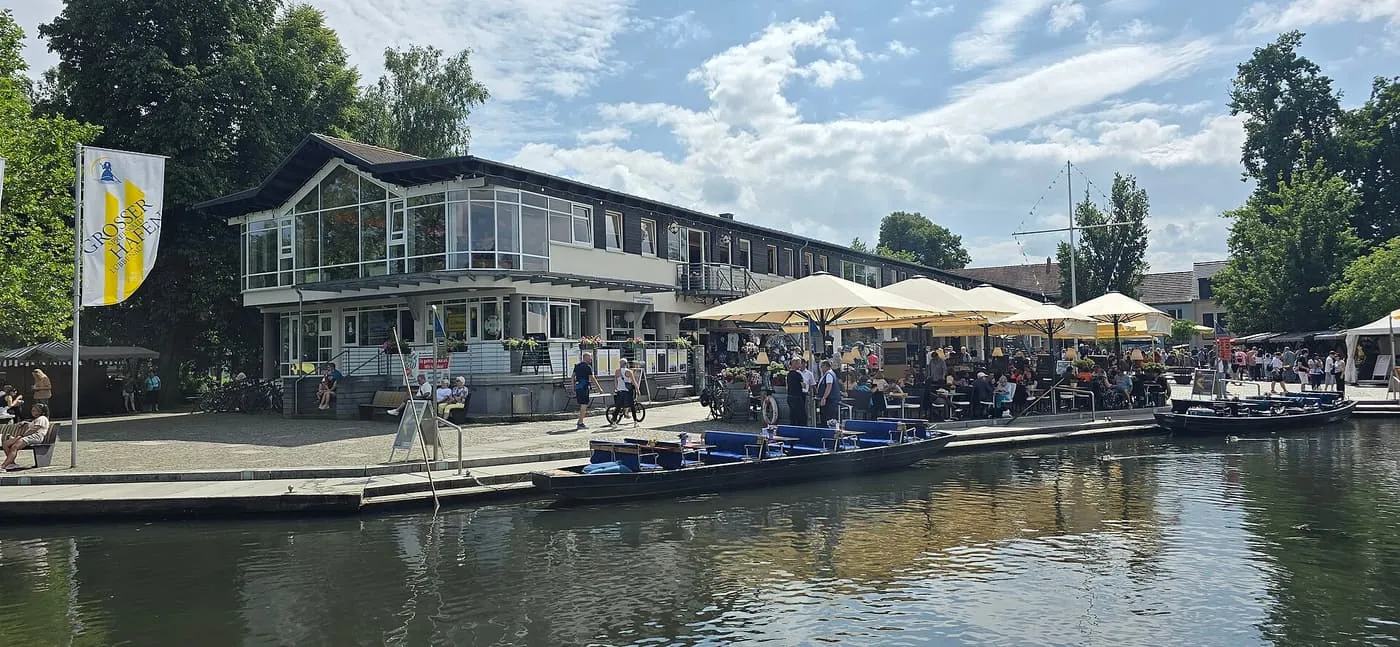 The Großer Spreewaldhafen building and its landing stage in Lübbenau, with punts moored alongside and cafe tables under parasols