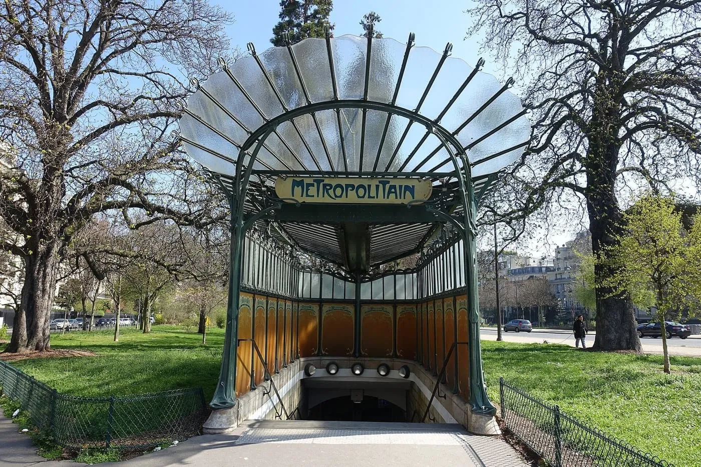 A green cast-iron and glass Art Nouveau metro entrance with a Métropolitain sign, standing on grass among trees at Porte Dauphine