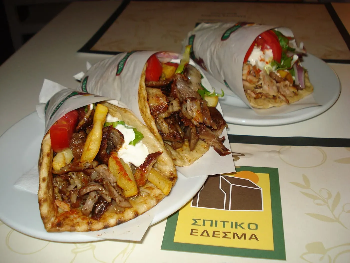 Two pork gyros and one chicken gyros wrapped in paper, each filled with shaved meat, chips, tomato and tzatziki