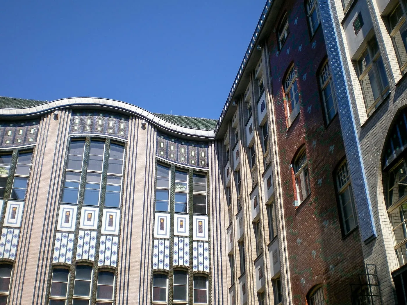 Glazed brick and tiled facades of the first courtyard of the Hackesche Höfe, with a wavy roofline against a blue sky