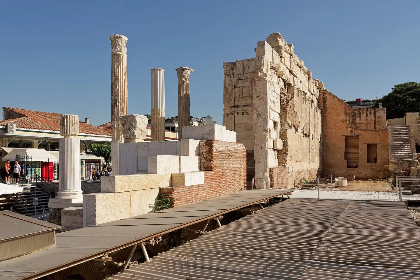 A few standing columns and the tall surviving wall of Hadrian's Library, with a metal walkway over the excavations in front