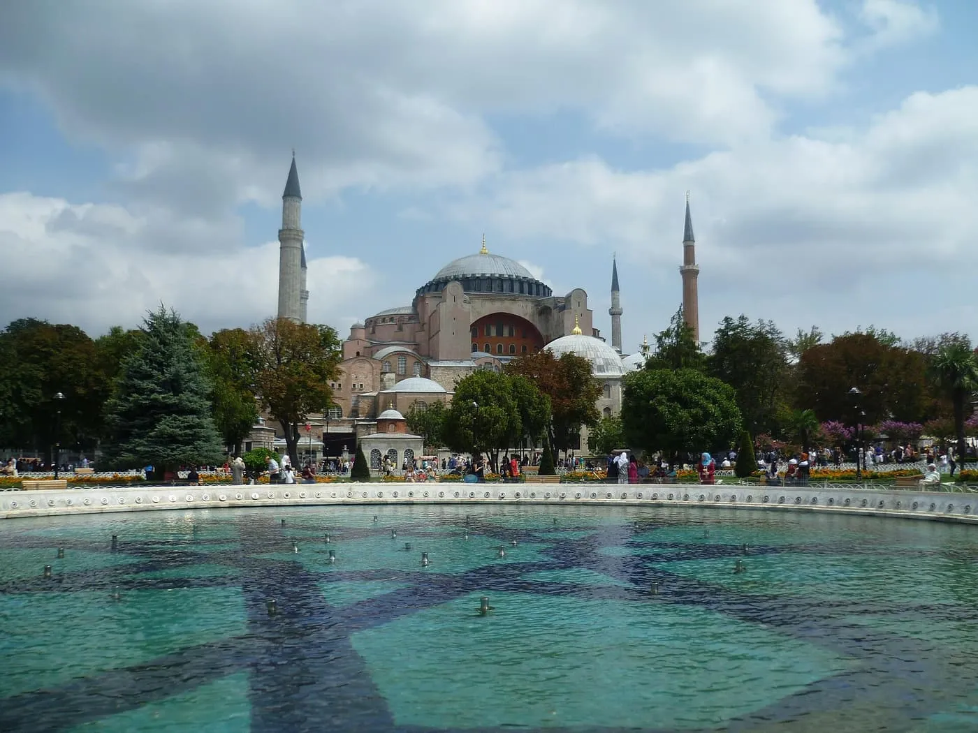 Hagia Sophia and its minarets seen across the turquoise basin of a fountain and the trees of Sultanahmet Square