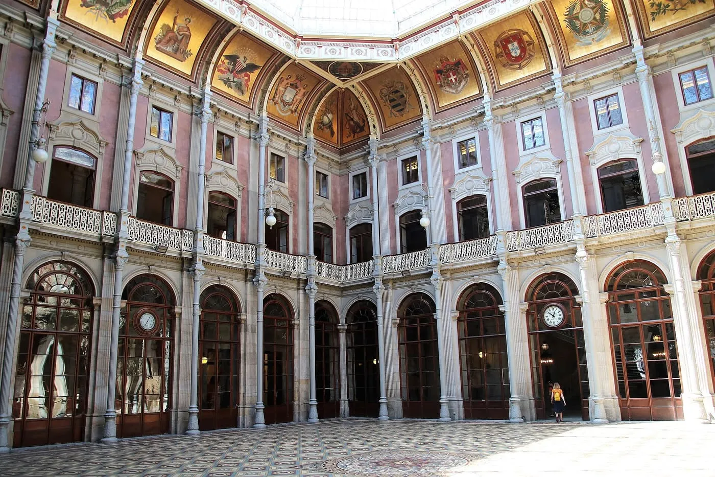 The Hall of Nations in the Palácio da Bolsa, a pink-walled courtyard under a glass roof ringed with painted coats of arms