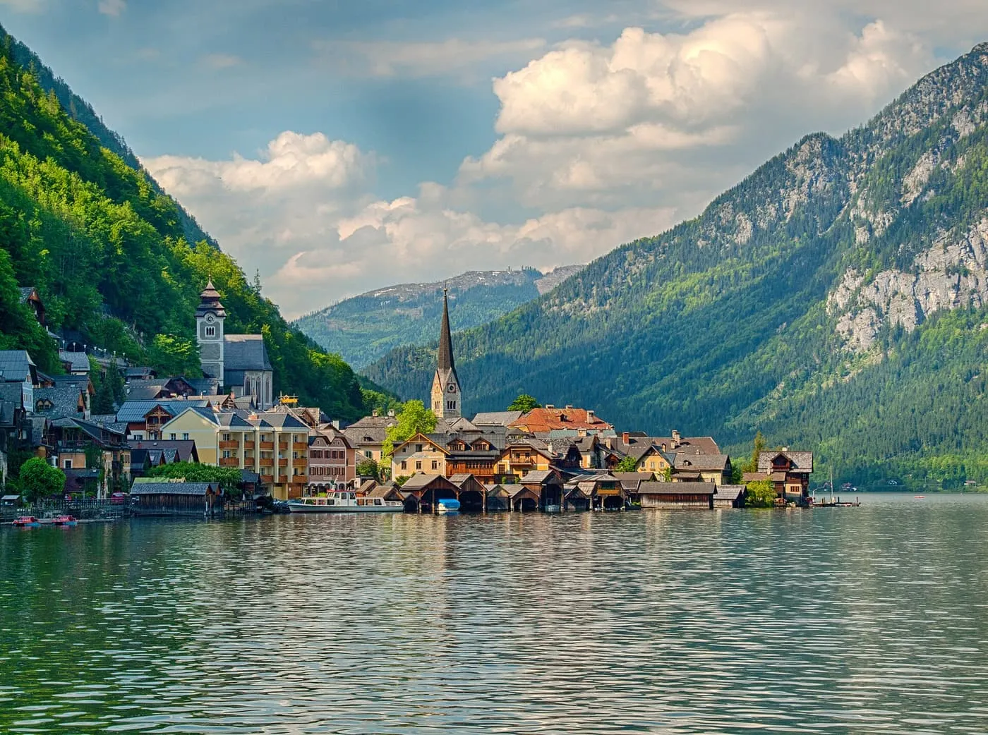 Hallstatt seen across the lake, with the church spire and boathouses at the water's edge below steep wooded mountains