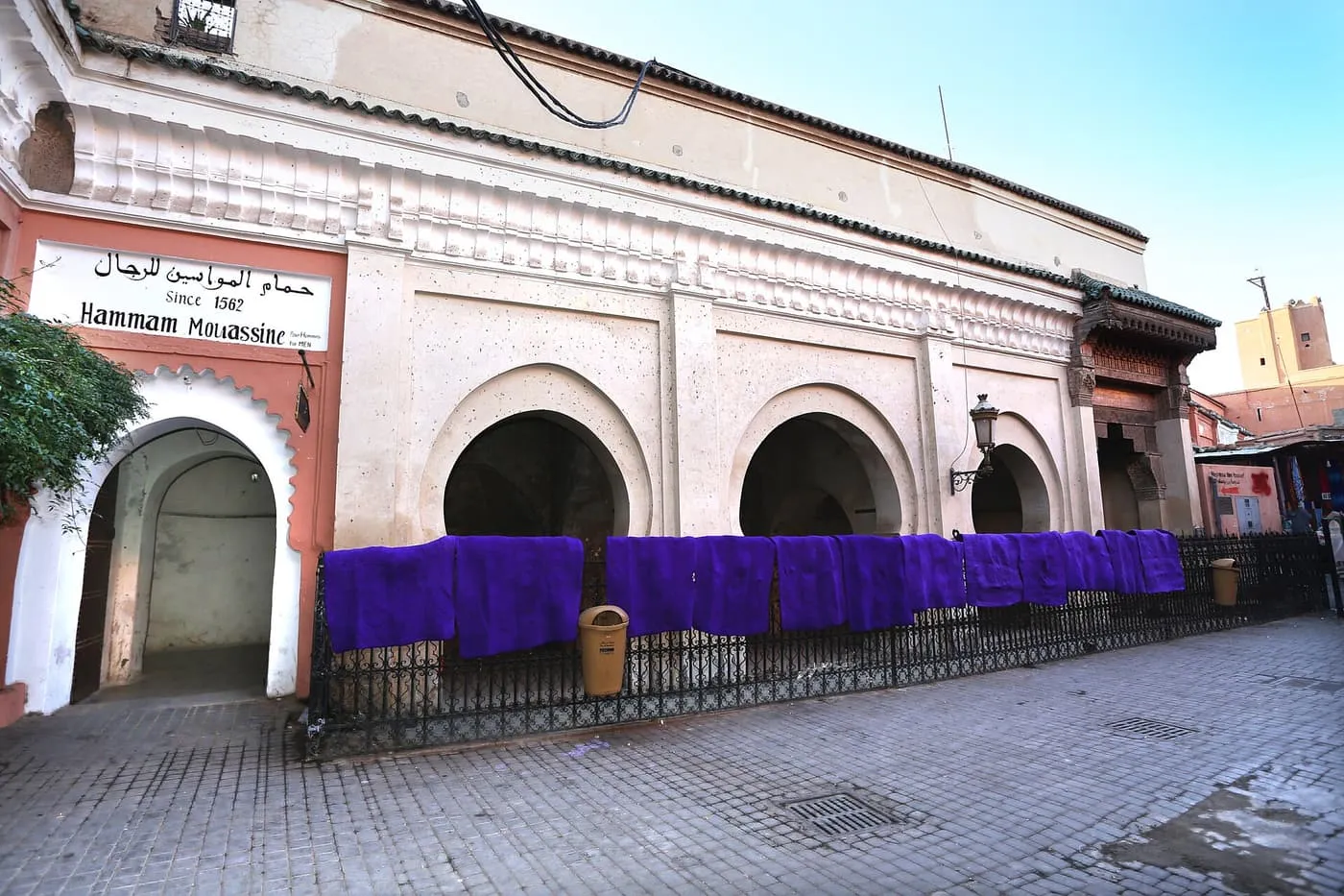 The men's entrance of Hammam Mouassine, a whitewashed arcade with a horseshoe-arched doorway and purple cloths hung over railings