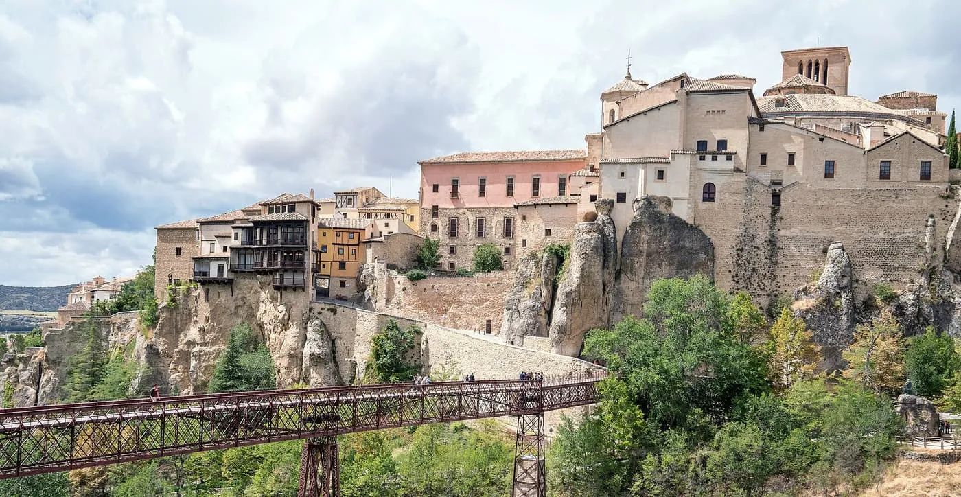 The Hanging Houses of Cuenca on the cliff edge above the Huécar gorge, with the iron San Pablo footbridge across the foreground