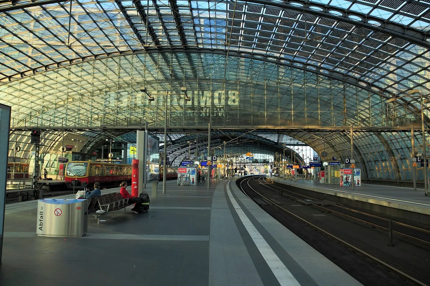 The glass-roofed platform hall of Berlin Hauptbahnhof, with an S-Bahn train at one platform and the tracks curving away