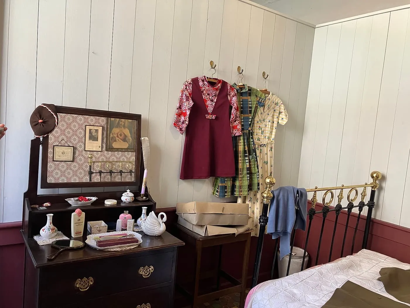 A furnished room at 14 Henrietta Street with a brass bed, a dressing table and dresses hanging on the wall