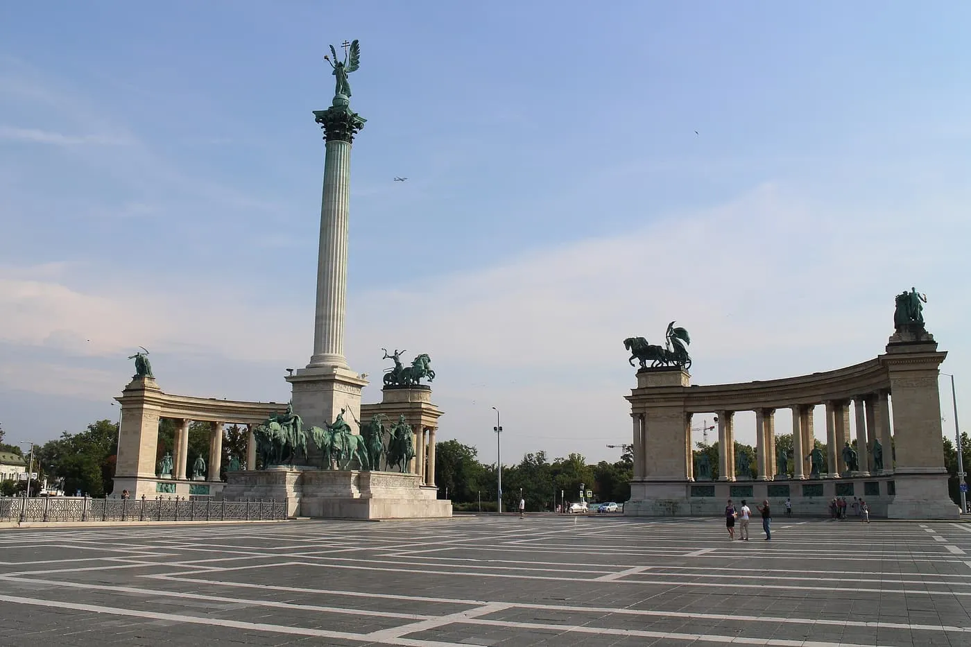 The Millennium Monument's tall column with the Archangel Gabriel on top, between two curved colonnades, across the paved Heroes' Square