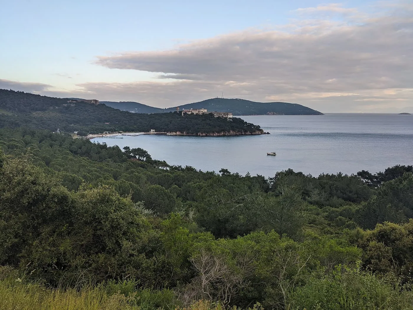 A calm bay fringed by pine woods on Heybeliada, with the old sanatorium building on the headland
