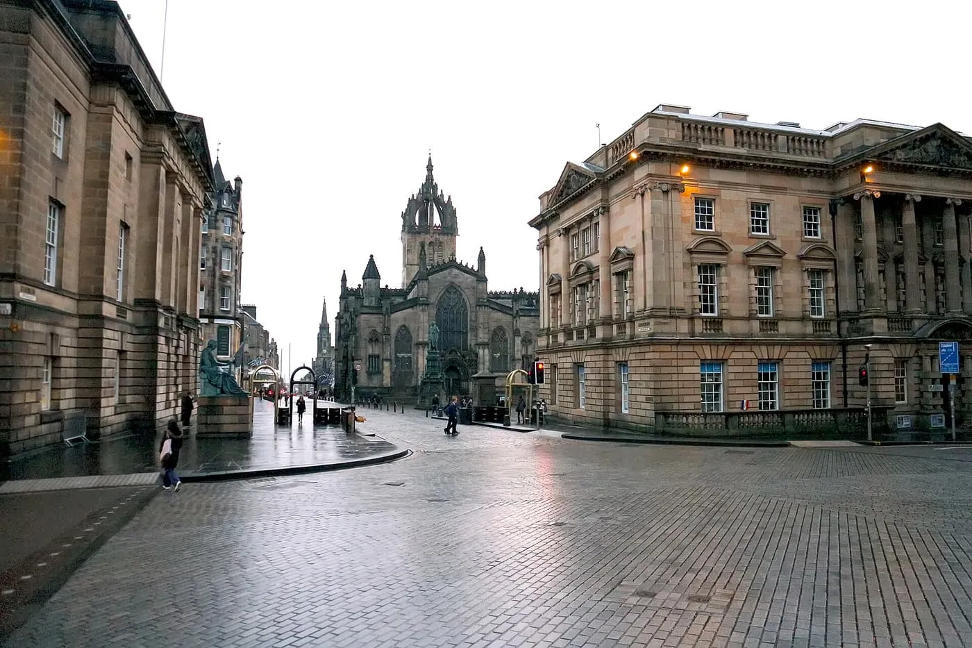A wet cobbled street between two grand stone buildings, with St Giles' Cathedral and its crown spire at the far end