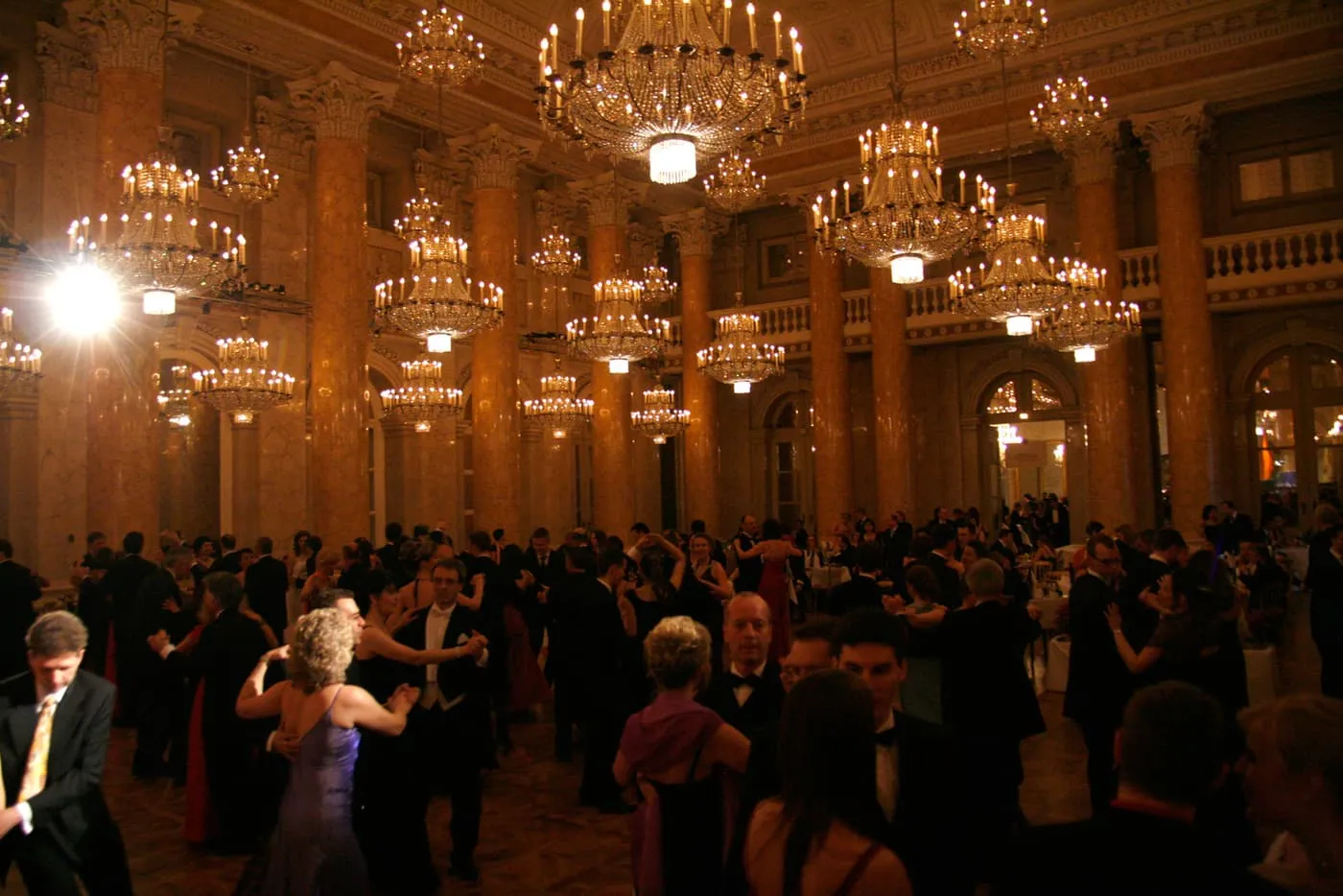 Couples waltzing under crystal chandeliers in the marble-columned Zeremoniensaal of the Hofburg