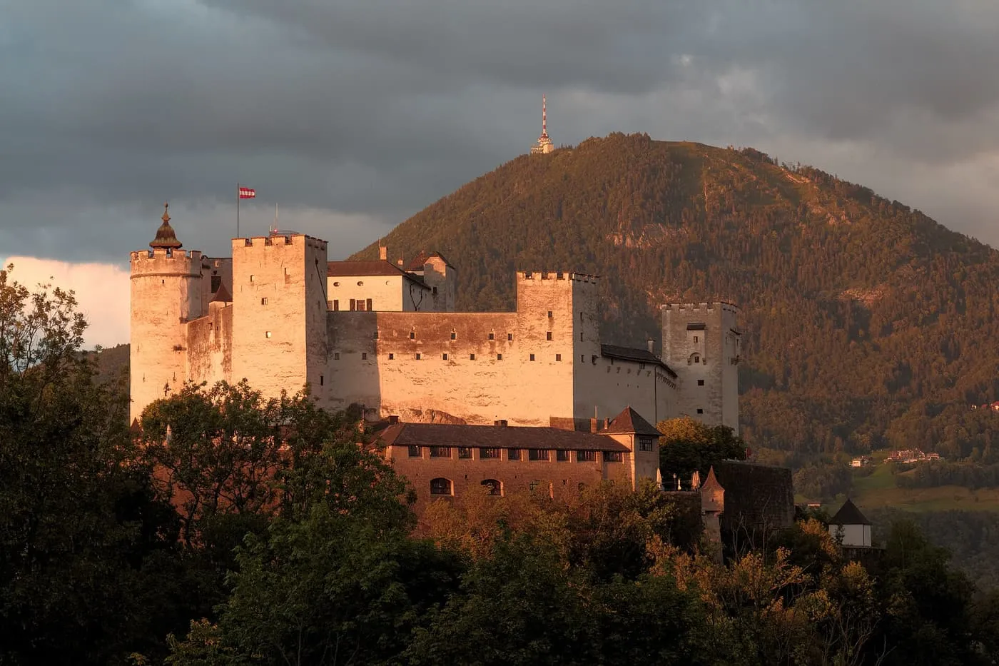 Hohensalzburg Fortress lit by evening sun, with a wooded mountain behind it
