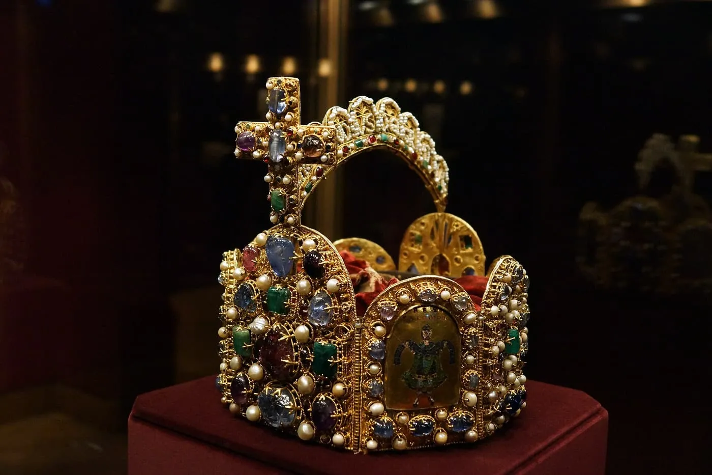 The Imperial Crown of the Holy Roman Empire, a gold crown set with pearls and gems, with an arch and cross, on a red cushion in a dark case