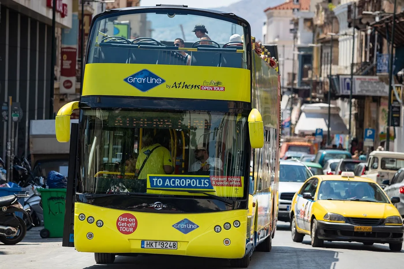 A yellow open-top Gray Line hop-on hop-off bus with a To Acropolis sign driving along a busy Athens street