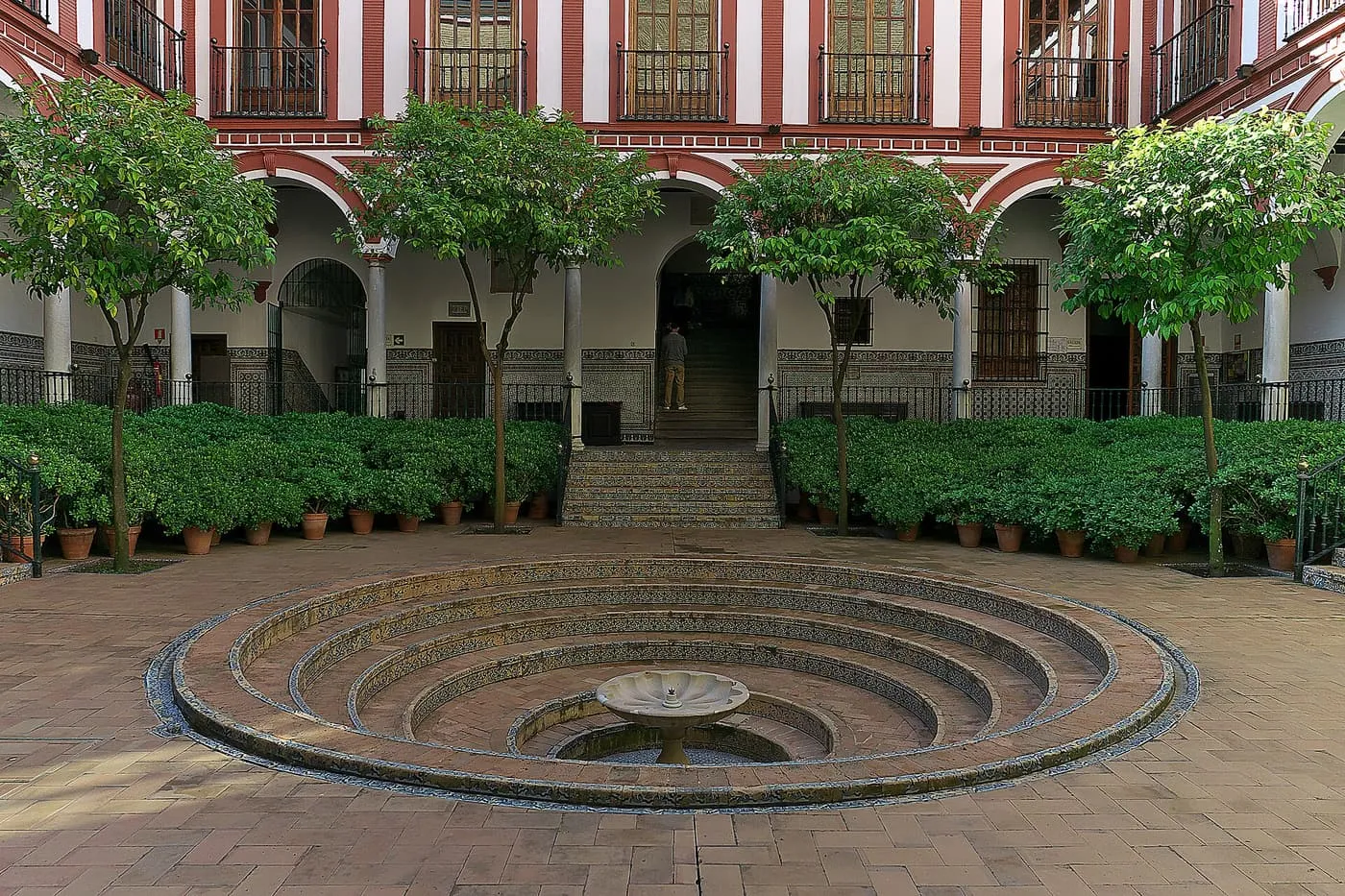 The courtyard of the Hospital de los Venerables, with a sunken circular fountain, orange trees and red and white striped walls