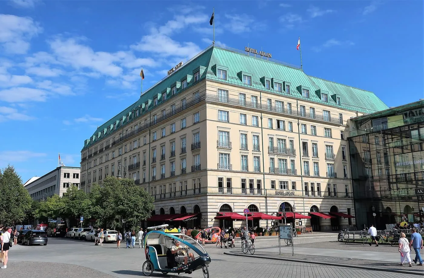 The cream stone facade and green copper roof of the Hotel Adlon Kempinski, with red awnings over its ground floor