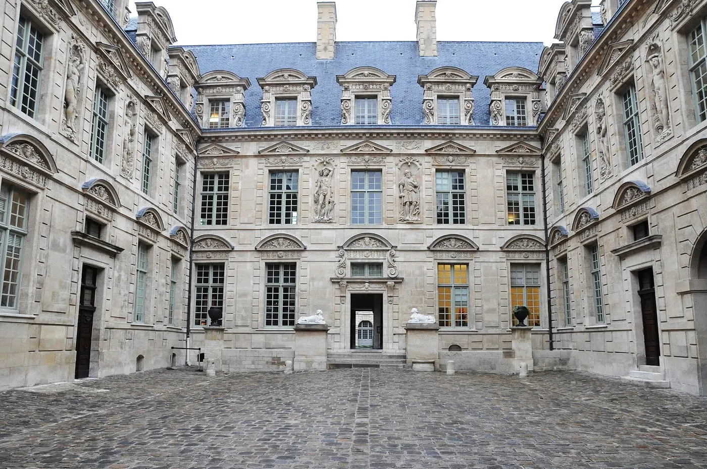 The paved courtyard of the Hôtel de Sully, with carved Renaissance façades on three sides under a blue slate roof