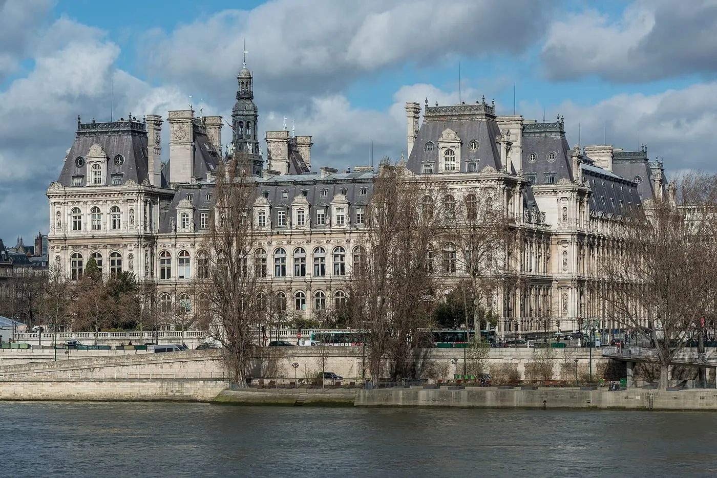 The Hôtel de Ville of Paris seen across the Seine, a long Renaissance-style building with steep grey roofs, a clock tower and many windows