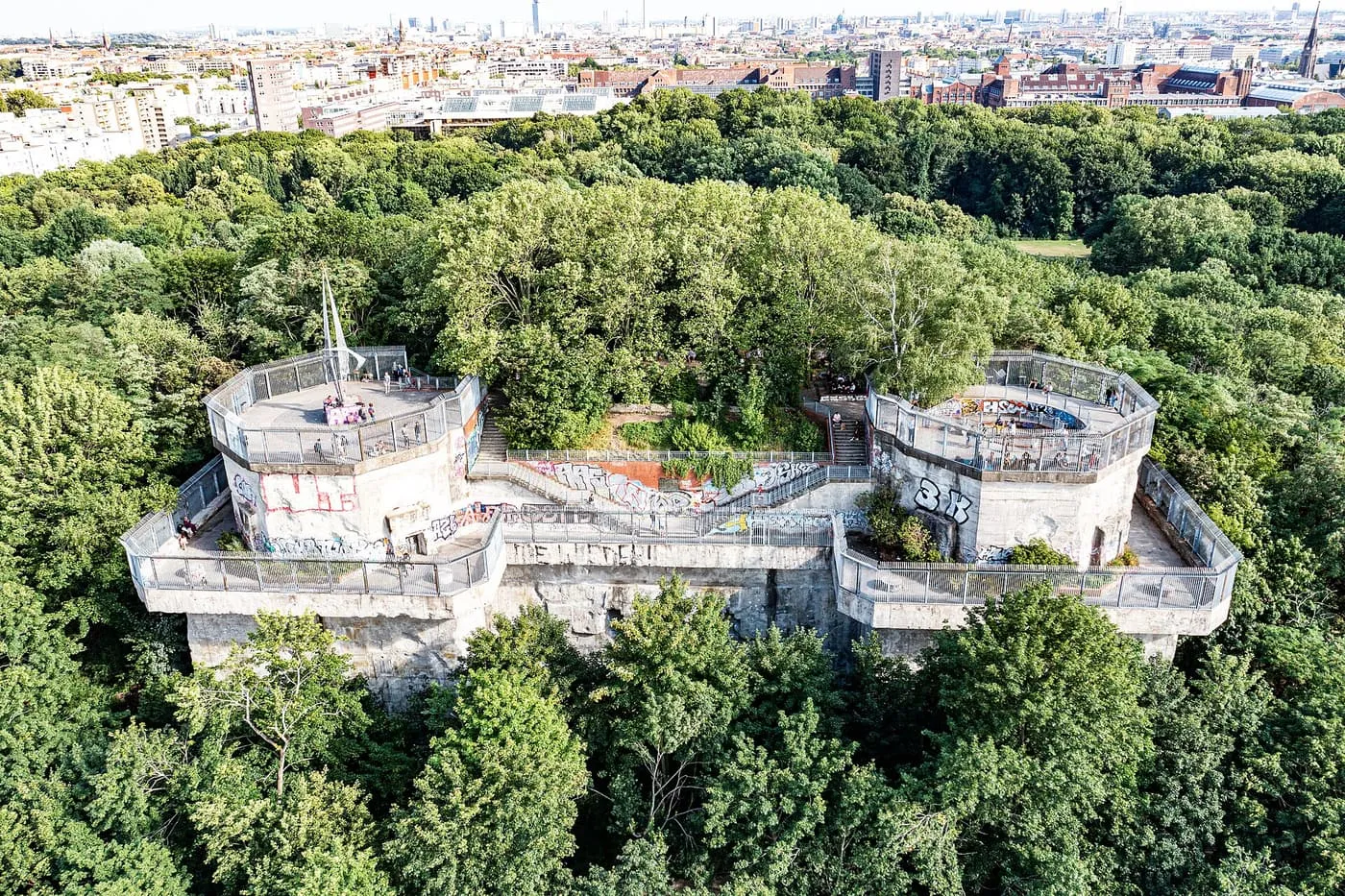 The Humboldthain flak tower from the air, a grey concrete block with two round gun platforms rising out of the trees of the park