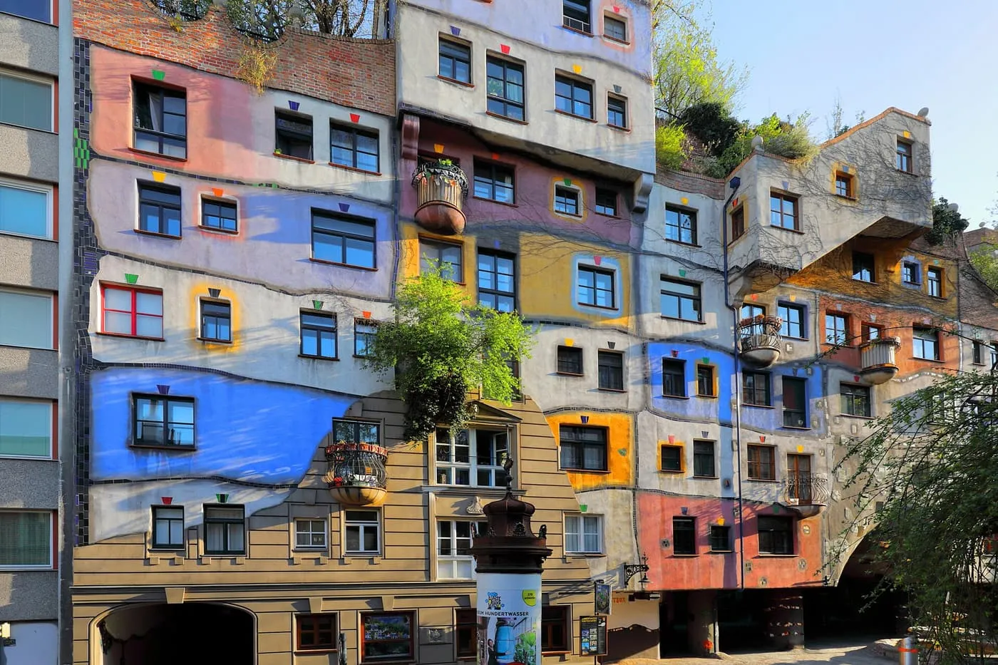 The Hundertwasserhaus façade, with uneven blocks of blue, yellow, red and grey, irregular windows and trees growing from the upper terraces