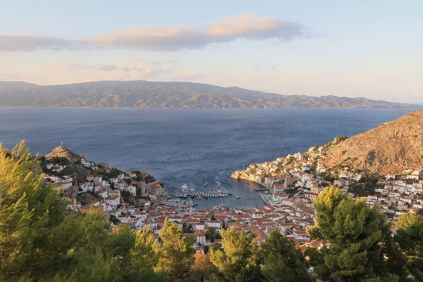 The small harbour of Hydra seen from the hillside above, with white and terracotta-roofed houses climbing both sides of the bay
