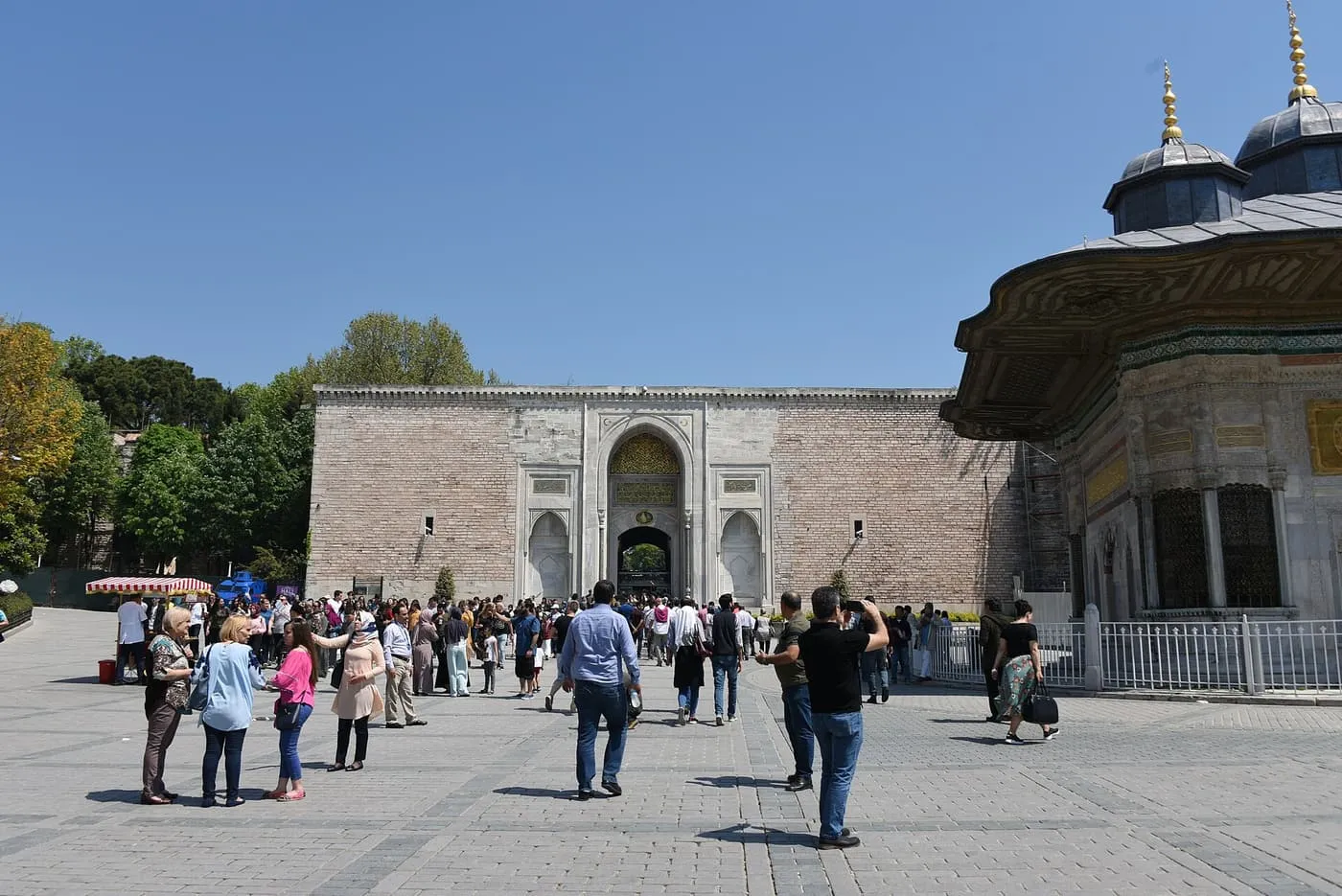 The Imperial Gate of Topkapı Palace in the palace wall, with the carved fountain of Ahmed III at right and visitors in the square