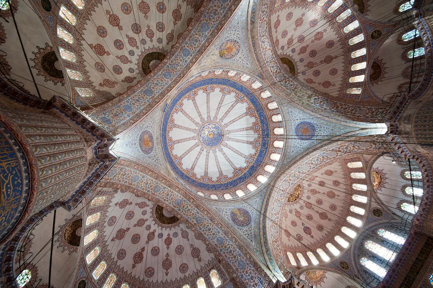 The interior of the Blue Mosque looking up at a cascade of half-domes, with painted and tiled surfaces and rows of small windows